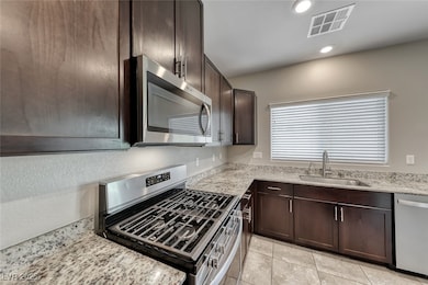 Kitchen with appliances with stainless steel finishes, dark brown cabinetry, light stone counters, recessed lighting, and light tile patterned flooring