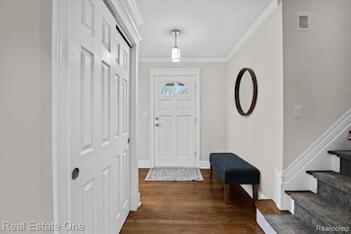 Entrance foyer with crown molding, dark wood-style flooring, and stairway