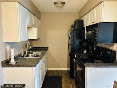 Kitchen with black appliances, dark countertops, dark wood finished floors, a textured ceiling, and white cabinetry