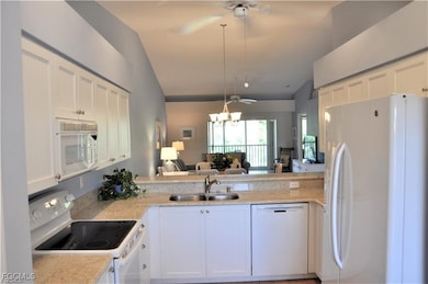 Kitchen featuring white appliances, white cabinets, open floor plan, a ceiling fan, and light stone counters