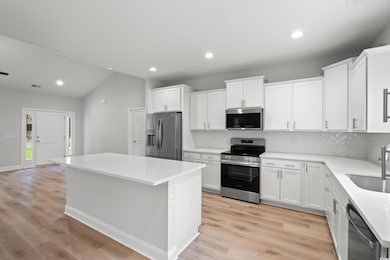 Kitchen featuring appliances with stainless steel finishes, vaulted ceiling, backsplash, recessed lighting, and white cabinets
