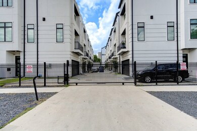 A modern living room with a sleek black sectional, gold-accented pillows, and two black chairs. It features a fireplace, a mounted TV, and large windows leading to a balcony, creating a bright and cozy space.