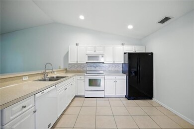Kitchen with white appliances, lofted ceiling, light countertops, light tile patterned floors, and backsplash