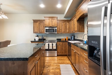 Kitchen featuring appliances with stainless steel finishes, brown cabinetry, light wood-style flooring, and decorative light fixtures
