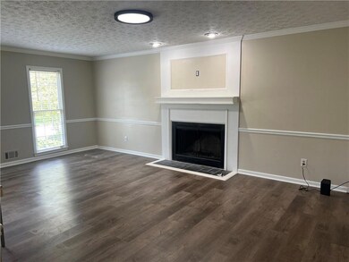 Unfurnished living room with a fireplace with raised hearth, wood finished floors, a textured ceiling, and ornamental molding