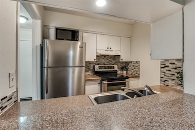 Kitchen featuring white cabinets, tasteful backsplash, appliances with stainless steel finishes, under cabinet range hood, and a textured wall