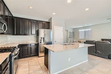 Kitchen with appliances with stainless steel finishes, open floor plan, light stone countertops, a kitchen island with sink, and light tile patterned floors