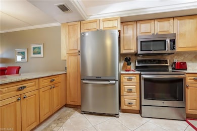 Kitchen featuring stainless steel appliances, crown molding, decorative backsplash, light tile patterned flooring, and light stone countertops