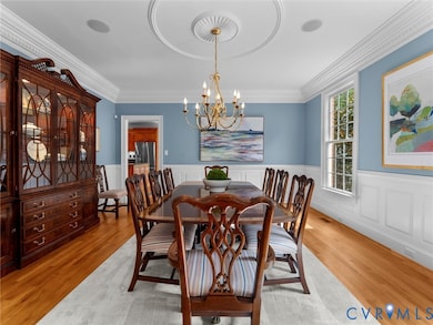 Dining space with a wainscoted wall, light wood-style floors, ornamental molding, a chandelier, and a decorative wall