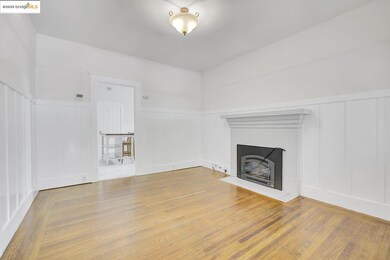 Unfurnished living room featuring a decorative wall, wood finished floors, a brick fireplace, and wainscoting