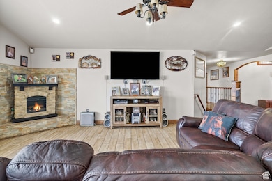 Living room featuring a ceiling fan, wood finished floors, a stone fireplace, baseboards, and arched walkways