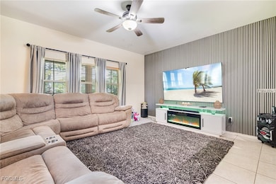 Living area featuring light tile patterned flooring, a ceiling fan, and an accent wall