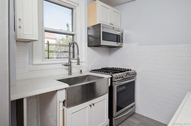 Kitchen with appliances with stainless steel finishes, tile walls, white cabinets, light wood-type flooring, and light stone counters