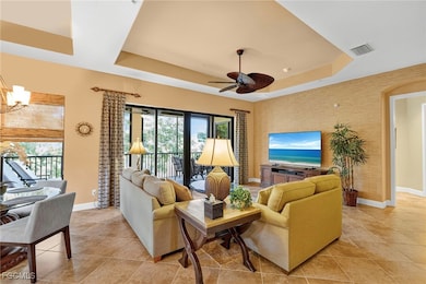 Living area with a tray ceiling, light tile patterned floors, a chandelier, and ceiling fan