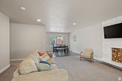 Living room featuring carpet, a stone fireplace, a textured ceiling, recessed lighting, and a chandelier