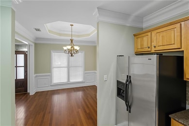 Kitchen with stainless steel fridge, a raised ceiling, ornamental molding, a chandelier, and dark wood-style floors