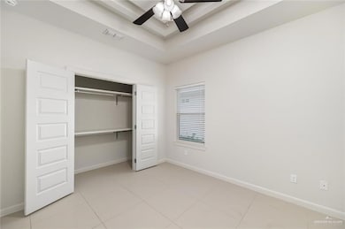Unfurnished bedroom featuring light tile patterned flooring, a closet, a ceiling fan, and a tray ceiling