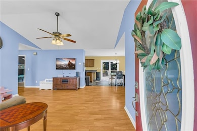 Living room with light wood-style floors, a ceiling fan, a chandelier, and vaulted ceiling