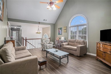 Living room with high vaulted ceiling, wood finished floors, a ceiling fan, a chandelier, and baseboards