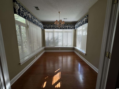 Unfurnished dining area with a chandelier, healthy amount of natural light, baseboards, a textured ceiling, and wood finished floors