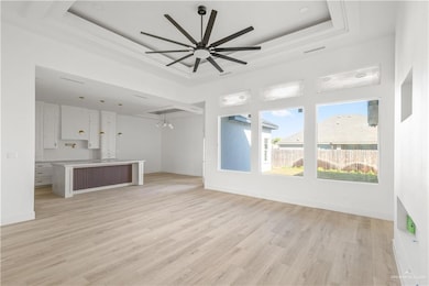 Unfurnished living room featuring a tray ceiling, light wood finished floors, a chandelier, and a ceiling fan