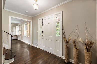 Foyer entrance featuring dark wood-style flooring, crown molding, baseboards, and stairway