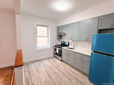 Kitchen featuring gray cabinets, freestanding refrigerator, stainless steel range with gas stovetop, decorative backsplash, and light stone counters