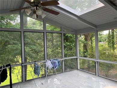 Unfurnished sunroom featuring view of wooded area, a ceiling fan, and a skylight