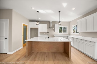 Kitchen featuring light wood-type flooring, white cabinets, light stone counters, decorative light fixtures, and an island with sink