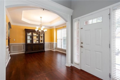 Entrance foyer with arched walkways, a chandelier, dark wood finished floors, wainscoting, and a raised ceiling
