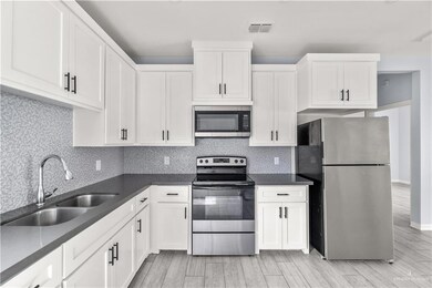 Kitchen featuring dark countertops, white cabinetry, appliances with stainless steel finishes, and a sink