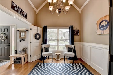 Living area with a chandelier, wood finished floors, high vaulted ceiling, crown molding, and wainscoting
