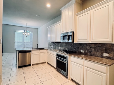 Kitchen featuring dark stone counters, tasteful backsplash, appliances with stainless steel finishes, decorative light fixtures, and a chandelier