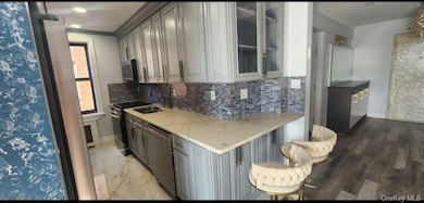 Kitchen with glass insert cabinets, tasteful backsplash, stainless steel appliances, light stone countertops, and crown molding