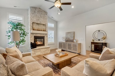 Living room with light wood-type flooring, a stone fireplace, ceiling fan, and high vaulted ceiling