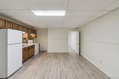 Kitchen with white appliances, light wood-type flooring, a paneled ceiling, light countertops, and brown cabinetry