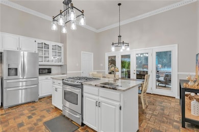 Kitchen featuring appliances with stainless steel finishes, brick floors, a sink, ornamental molding, and a kitchen island with sink