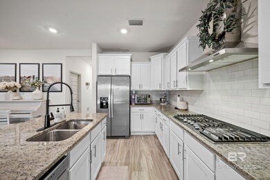 Kitchen featuring appliances with stainless steel finishes, wall chimney exhaust hood, white cabinets, light stone countertops, and light wood-type flooring