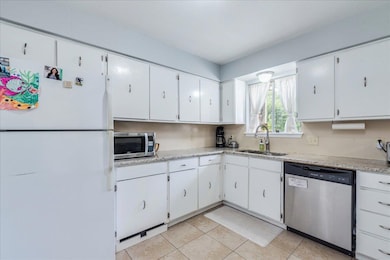 Kitchen with a sink, white cabinetry, light tile 