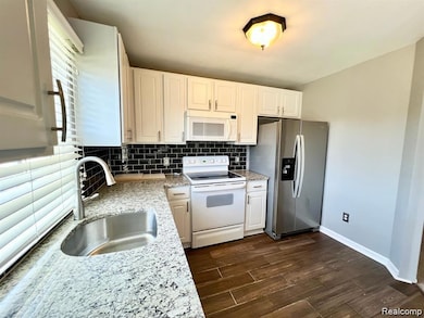 Kitchen featuring decorative backsplash, white appliances, light stone countertops, white cabinets, and dark wood-type flooring