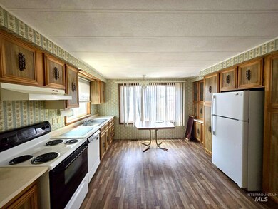 Kitchen with white appliances, under cabinet range hood, wallpapered walls, brown cabinets, and dark wood-style floors