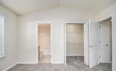Unfurnished bedroom featuring a spacious closet, a closet, carpet flooring, vaulted ceiling, and ensuite bath