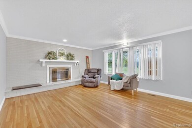 Sitting room with ornamental molding, wood finished floors, a brick fireplace, and a textured ceiling