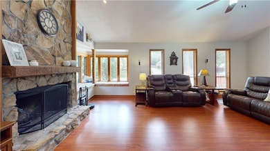 Living room featuring wood finished floors, vaulted ceiling, a stone fireplace, and ceiling fan