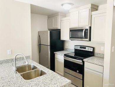 Kitchen with appliances with stainless steel finishes, light stone countertops, and white cabinetry