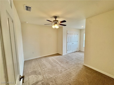 Empty room with carpet floors, a ceiling fan, visible vents, and baseboards