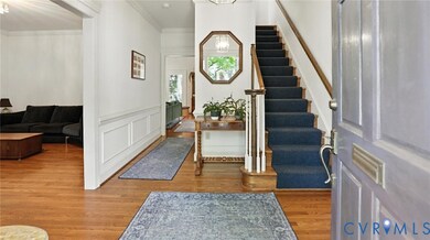 Foyer entrance featuring wood finished floors, crown molding, a wainscoted wall, a decorative wall, and stairs