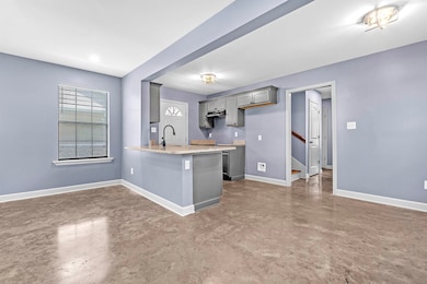 Kitchen featuring gray cabinetry, finished concrete floors, a peninsula, and under cabinet range hood