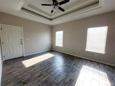 Unfurnished room with a raised ceiling, ceiling fan, and dark wood finished floors