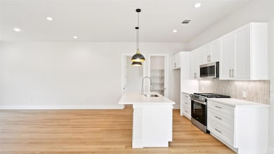 Kitchen featuring white cabinets, appliances with stainless steel finishes, hanging light fixtures, recessed lighting, and a kitchen island with sink